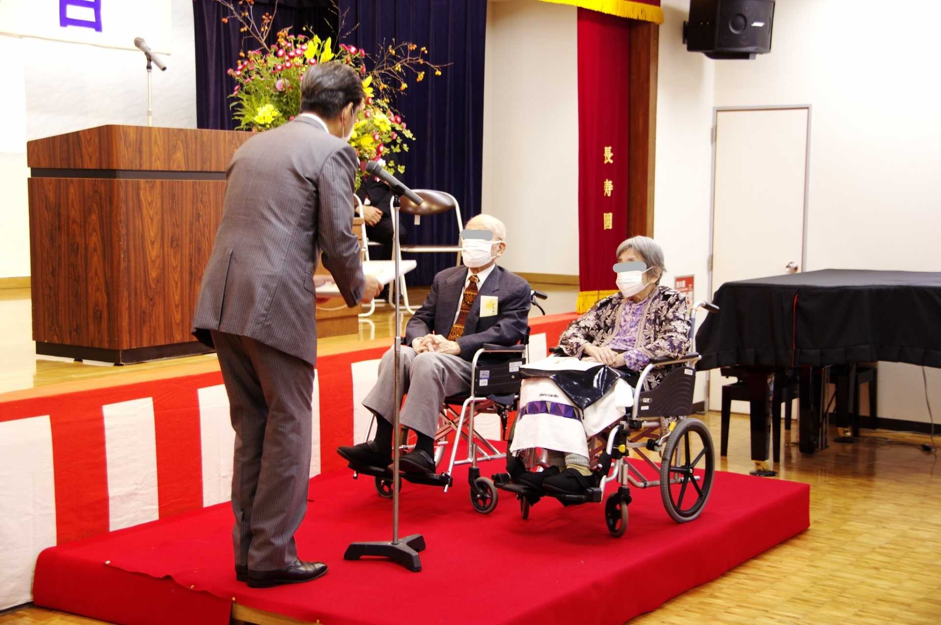 施設内のイベント。舞台上で演技者と車椅子の入居者が交流している風景。