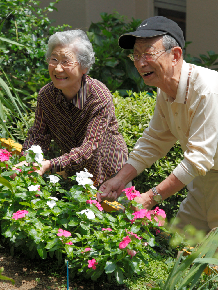 高齢の入居者2名が施設の庭で花の手入れをしている生活風景