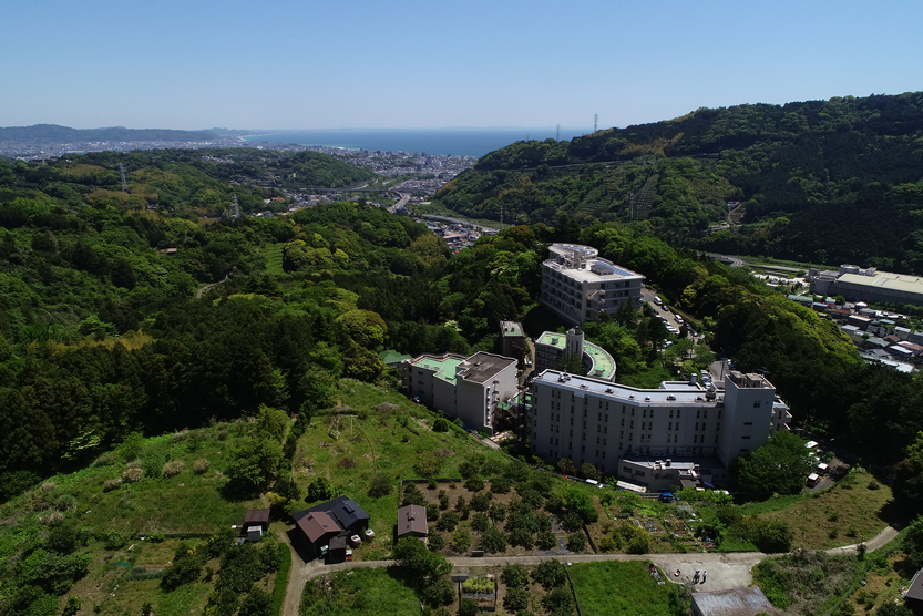 緑豊かな丘陵地に立つ介護施設の外観。広々とした敷地と周辺景観が見える。